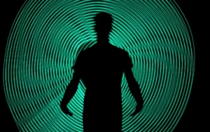 Silhouette of a person standing in front of concentric glowing teal light rings, symbolising restricted advertising