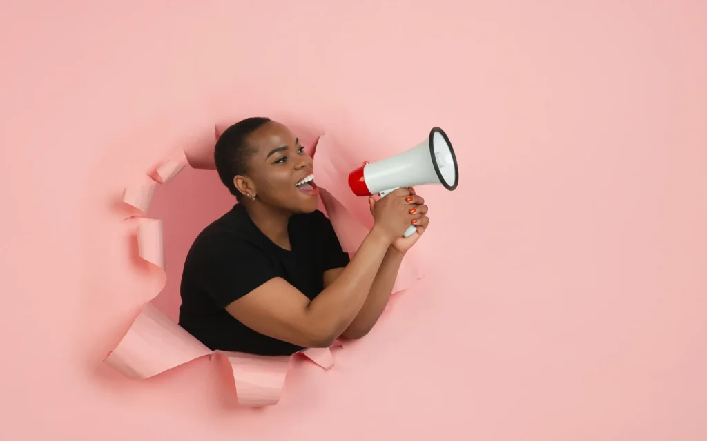 Person emerging through torn pink paper holding a megaphone to symbolise bold communication by Ottmann-Polignac.
