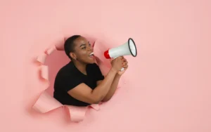 Person emerging through torn pink paper holding a megaphone to symbolise bold communication by Ottmann-Polignac.