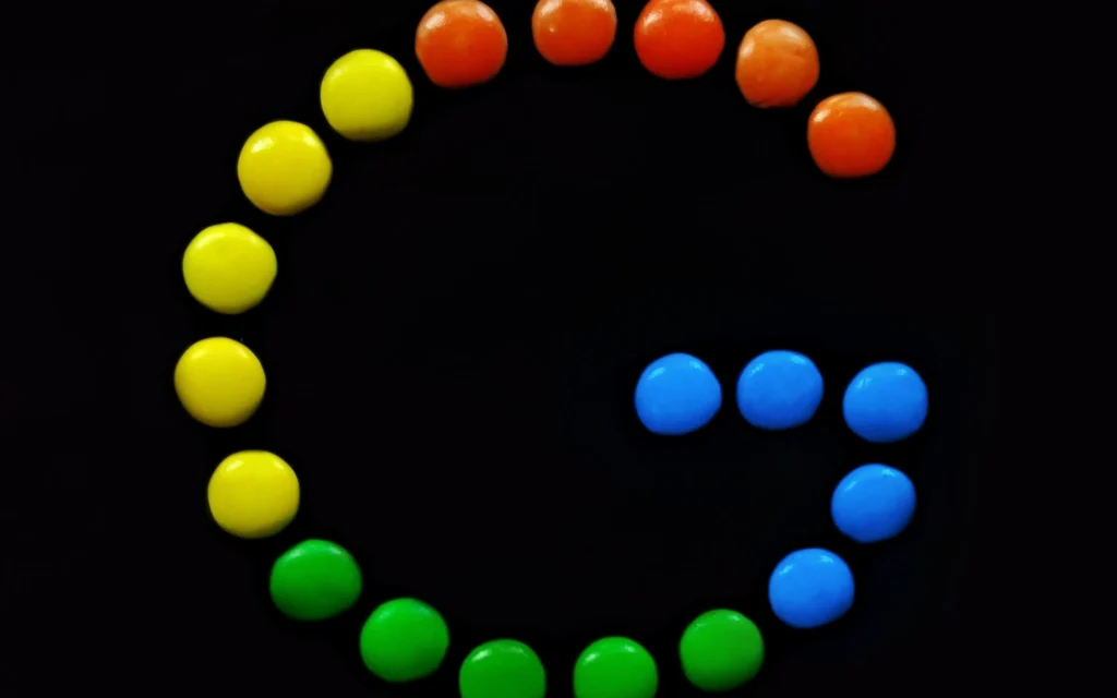 Coloured sweets arranged in the shape of the Google ‘G’ logo against a dark background.