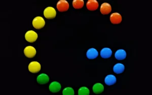 Coloured sweets arranged in the shape of the Google ‘G’ logo against a dark background.